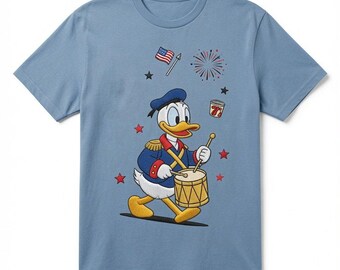 May include: A dusty blue short-sleeve t-shirt featuring a graphic of Donald Duck dressed in a blue and red marching band uniform, playing a yellow drum. The design includes a small American flag, a firework, red stars, and a 7-Up soda cup.