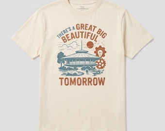 May include: A cream-colored short-sleeve t-shirt featuring a graphic print of a futuristic building, a sun, and gears. The text reads "THERE'S A GREAT BIG BEAUTIFUL TOMORROW" in blue and orange lettering, with "THE TOMORROW CO." printed on the inner neck.