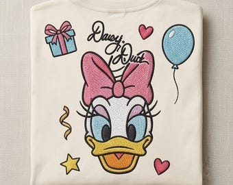 May include: A cream-colored t-shirt featuring an embroidered graphic of Daisy Duck's face with a pink bow, surrounded by a blue gift box, a blue balloon, two small pink hearts, a yellow star, and a gold ribbon. The text Daisy Duck is embroidered above.