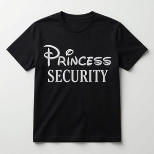 Może przedstawiać: Czarna koszulka z krótkim rękawem z białym haftowanym napisem Princess Security z przodu. Słowo Princess zostało napisane stylizowaną kursywą, natomiast słowo Security zostało napisane pogrubioną czcionką szeryfową wielkimi literami.