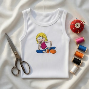 May include: White ribbed tank top with an embroidered cartoon character in a seated pose. The character has blonde hair, a pink top, blue pants, and orange shoes. A red pin cushion, scissors, and spools of thread are also visible.