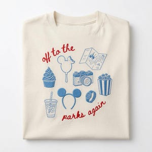 Könnte beinhalten: Ein cremefarbenes T-Shirt mit blauen Stickereien von einem Softeis, einem mausförmigen Luftballon, einer Karte, einer Kamera, einem Getränk, Mausohren, einer Uhr und Popcorn. Der rote Sticktext lautet off to the parks again.