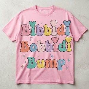 May include: A light pink short-sleeve t-shirt featuring the text Bibbidi Bobbidi Bump in large, colorful, rounded letters. Each letter has a small mouse-ear shape on top. The design includes small star icons scattered around the text.