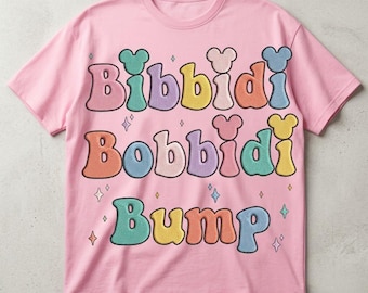 May include: A light pink short-sleeve t-shirt featuring the text Bibbidi Bobbidi Bump in large, colorful, rounded letters. Each letter has a small mouse-ear shape on top. The design includes small star icons scattered around the text.