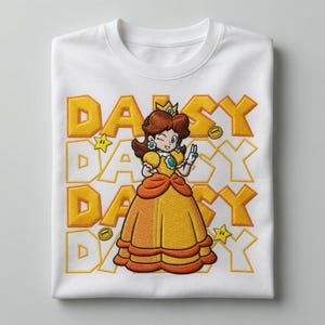 Pode incluir: Uma t-shirt branca com um gráfico central de uma personagem de cabelo castanho com um vestido amarelo e laranja, a piscar o olho e a fazer o sinal de paz. O fundo consiste no texto amarelo DAISY repetido, com pequenas estrelas e moedas.