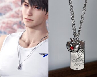 Puede incluir: Collar plateado con un colgante de chapa de identificación y un charm de manzana. La chapa de identificación tiene grabadas las palabras "I come back". El charm de manzana tiene una gema roja. El collar se lleva sobre una camiseta sin mangas blanca.