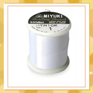Puede incluir: Un carrete de hilo blanco para abalorios Miyuki. La etiqueta dice "MIYUKI Beading Thread 330dtex 100% Nylon Made in Japan". El carrete es blanco con base y parte superior blancas. También se ve el texto "LOT TM1OR COL 1".