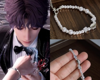 May include: A pearl bracelet with a silver seashell and crystal accents. The bracelet features a mix of small and large white pearls. The bracelet is shown on a wooden surface and on a person's wrist.