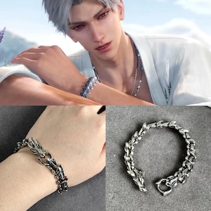 May include: A silver-colored bracelet with a dragon-scale design. The bracelet is made of metal and features a detailed, articulated design. The clasp is a simple hook and eye closure. The bracelet is shown on a wrist and also on a gray surface.