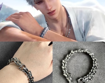 Puede incluir: Una pulsera plateada con un diseño de escamas de dragón. La pulsera está hecha de metal y presenta un diseño detallado y articulado. El cierre es un simple cierre de gancho y ojo. La pulsera se muestra en una muñeca y sobre una superficie gris.