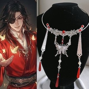 May include: A silver-toned metal choker necklace featuring an intricate filigree design, a central butterfly pendant, and dangling elements. The piece is adorned with small red beads, white faux pearls, and long, smooth red teardrop-shaped charms.