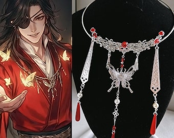 Puede incluir: Un collar tipo gargantilla de metal plateado con un diseño de filigrana intrincado, un colgante de mariposa central y elementos colgantes. La pieza está adornada con pequeñas cuentas rojas, perlas artificiales blancas y largos dijes rojos.