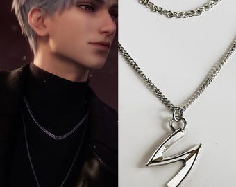 Puede incluir: Un collar plateado con un diseño de cadena en capas. La cadena inferior presenta un colgante con la forma de la letra "S". El collar se muestra sobre un fondo blanco y también lo lleva una persona en la imagen.
