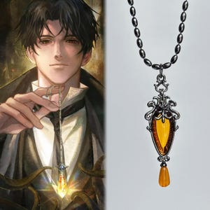 May include: A silver-toned necklace featuring an elongated, teardrop-shaped amber-colored pendant encased in an ornate, filigree metal frame. The pendant includes a smaller, dangling amber-colored bead at the base and hangs from a simple silver chain.