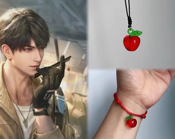 Puede incluir: Un colgante de manzana de cristal rojo con una hoja verde en un collar de cordón negro y una pulsera de cordón rojo a juego con un dije de manzana de cristal. Los dijes de manzana tienen un acabado brillante y una pequeña hoja verde.