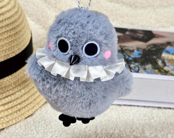 May include: A plush gray bird with large black eyes, pink cheeks, and a white ruffled collar. The bird has a black beak and feet, and a silver chain for hanging. The bird is a cute, whimsical design.