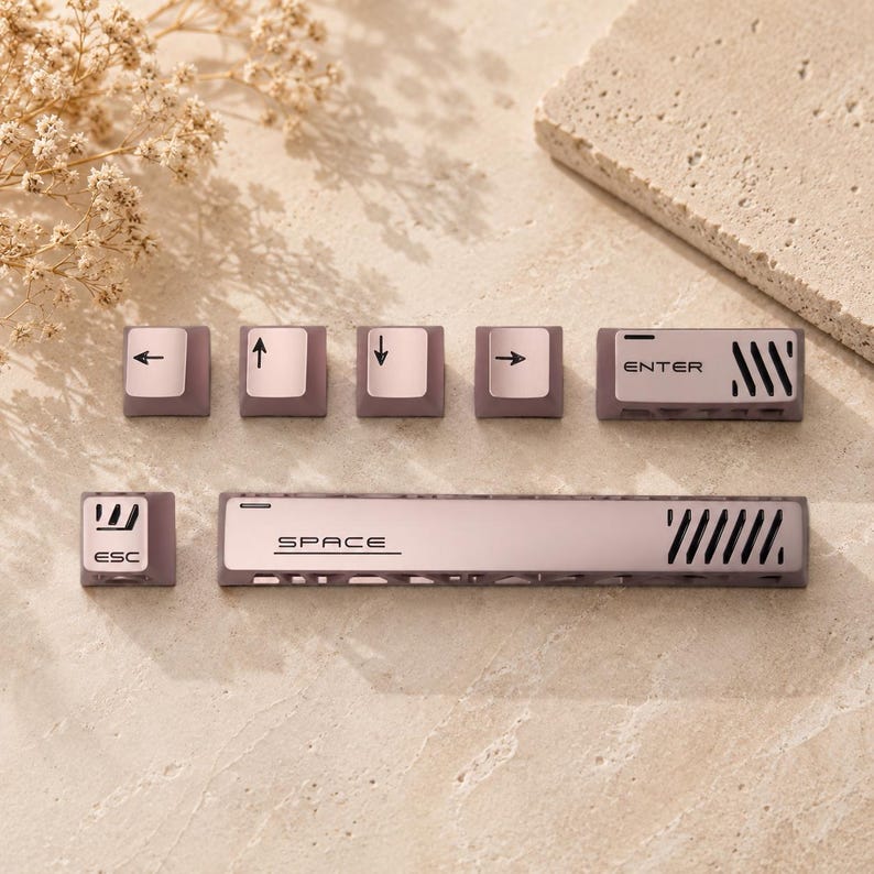 May include: A set of mauve mechanical keyboard keycaps including an ESC key, a space bar, an ENTER key, and four arrow keys. Each keycap features a smooth finish with black printed text and icons, including directional arrows and labels.