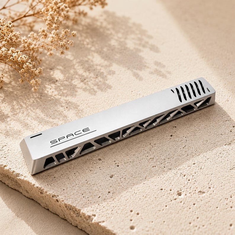 May include: A silver-coloured rectangular metal bar with the word SPACE printed on the top surface. The object features a series of triangular cutouts along the side and a row of vertical slits at one end, creating a structured, industrial appearance.