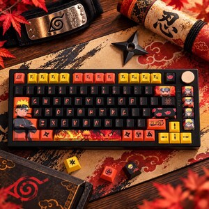 May include: A black mechanical keyboard featuring custom keycaps with Naruto anime graphics, including character illustrations, shuriken symbols, and red cloud patterns. The keys have a black, yellow, and orange color scheme with a rotary knob.