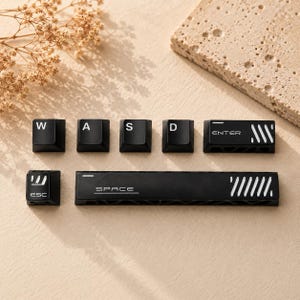 May include: A set of black mechanical keyboard keycaps including W, A, S, D, Enter, Esc, and a long Space bar. Each keycap features white lettering and distinct white graphic accents, with the Enter and Space keys displaying diagonal line patterns.