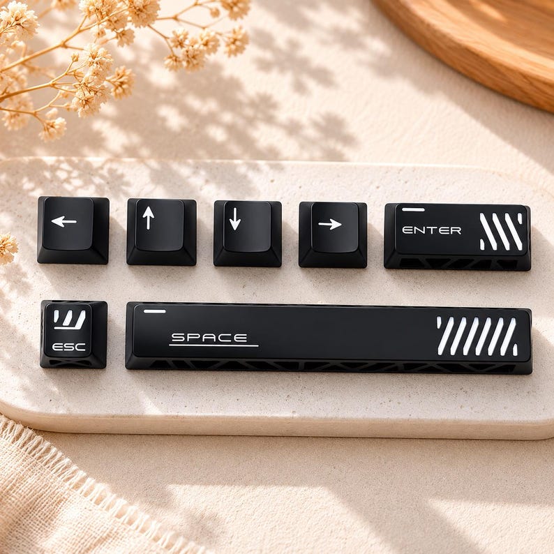 May include: A set of black mechanical keyboard keycaps featuring white icons and text. The collection includes arrow keys, an ESC key with a graphic, an ENTER key with diagonal stripes, and a long SPACE bar with a linear design and text.