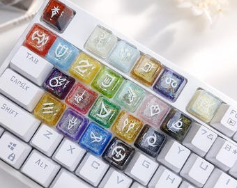 May include: A white mechanical keyboard featuring a collection of custom resin keycaps. Each keycap is translucent, filled with colourful glitter, and displays a unique white engraved symbol. The keys are arranged in a grid pattern.