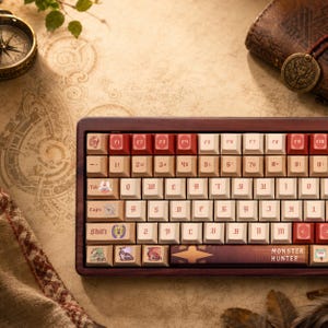 Op de afbeelding: Een mechanisch toetsenbord met een donkerhouten frame en crèmekleurige toetsen met rode accenten. De toetsen tonen een aangepast gotisch lettertype en diverse monsterpictogrammen, met de tekst "MONSTER HUNTER" op de spatiebalk.