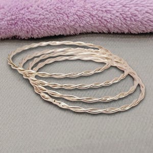 May include: A set of four thin, circular bangles made of polished silver-toned metal. Each bangle features a continuous twisted rope texture that creates a repeating spiral pattern along the entire circumference of the jewellery piece.