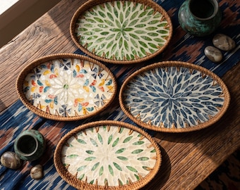 Könnte beinhalten: Vier ovale Tabletts mit geflochtenen Rattanrändern und eingelegten Muschelmosaikmustern. Die Designs zeigen grüne, blaue und mehrfarbige blütenartige Blütenblattmotive, die in radialen Mustern auf einem hellen Hintergrund angeordnet sind.