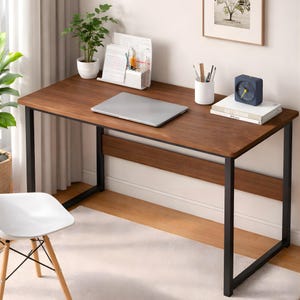 May include: A dark brown desk with black metal legs. A closed laptop, books, a clock, and stationery are on the desk. A white chair is in front, and a plant is in the background. The desk is approximately 120 cm long.