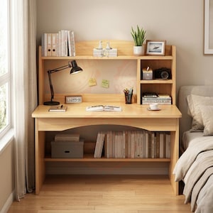 May include: A light-coloured wooden desk featuring an integrated hutch with multiple shelves, a flat work surface, and a lower storage shelf. The desk includes a black adjustable lamp, books, a small potted plant, a picture frame, and stationery.