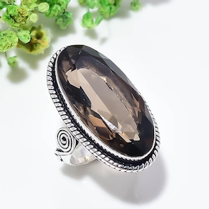 Könnte beinhalten: Ein Silberring mit einem großen, facettierten, oval geschliffenen Rauchquarz-Edelstein. Die Fassung verfügt über einen gedrehten, seilartigen Rand und ein dekoratives Spiraldetail an der Seite der Ringschiene mit polierter Metalloberfläche.