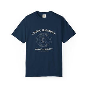 May include: Navy blue t-shirt with the words "COSMIC ALIGNMENT" above a graphic of hands, sun, and moon. The text "TRUST THE UNIVERSE" is below the graphic. The shirt is a short-sleeved crew neck.