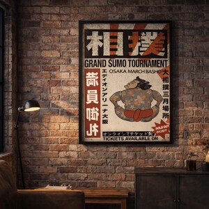 Puede incluir: Un póster vintage enmarcado que anuncia un Gran Torneo de Sumo en Osaka. El póster presenta una ilustración de luchador de sumo y texto japonés. El póster se muestra en una pared de ladrillo, junto a una ventana y una lámpara.