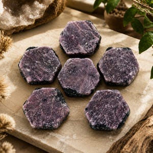 May include: Six hexagonal-shaped raw ruby crystals arranged in a circular pattern. Each stone features a deep purple and magenta hue with a textured, crystalline surface and dark, opaque edges, showcasing natural mineral formations.