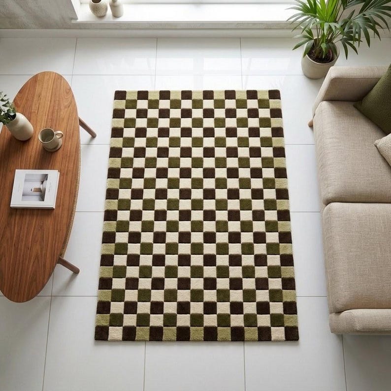 Op de afbeelding: Een rechthoekig vloerkleed met een dambordpatroon in bruin, groen en cr&egrave;me. Het kleed ligt op een witte tegelvloer, met een houten salontafel en een beige bank op de achtergrond. Het kleed voegt een geometrisch designelement toe aan de kamer.