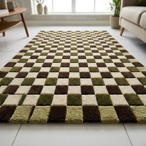 Op de afbeelding: Een rechthoekig vloerkleed met een dambordpatroon. Het kleed heeft afwisselende vierkanten in bruin, olijfgroen en cr&egrave;me. Het kleed is gemaakt van een zacht, pluche materiaal en ligt op een witte tegelvloer.