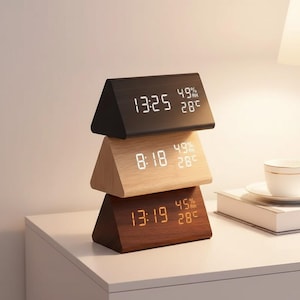 May include: Three triangular digital clocks stacked on a white surface. The top clock is black, the middle is light wood, and the bottom is dark wood. Each clock displays the time, humidity, and temperature in degrees Celsius.