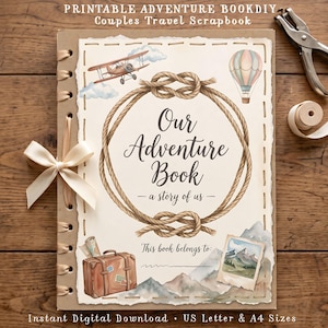 May include: A scrapbook with a cream-colored cover featuring a rope knot frame, a vintage airplane, a hot air balloon, a suitcase, and mountain illustrations. The text reads Our Adventure Book - a story of us - and This book belongs to.