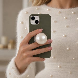 May include: A matte olive green smartphone case featuring a large, round, white faux pearl attachment centred on the back. The case has a dual-camera cutout in the top left corner and a smooth, solid-coloured finish for a clean, functional look.
