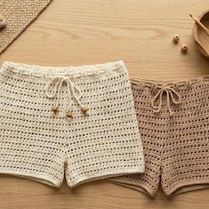 Può includere: Due pantaloncini all'uncinetto, uno color crema e uno color marrone chiaro, caratterizzati da un motivo a maglia aperta, vita elasticizzata con coulisse e piccole perline di legno alle estremità dei cordini sul modello crema, con una targhetta.