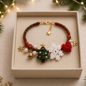 May include: A braided red and green cord bracelet featuring gold-tone metal charms including a bell, a star, and snowflakes. The bracelet is adorned with a crocheted green Christmas tree, a white crocheted snowflake, and a red crocheted heart.