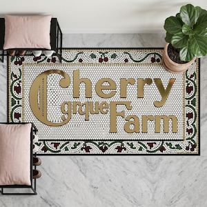 May include: A rectangular doormat with the words "Cherry Grove Farm" in gold lettering. The mat has a white background with a black and gold border, and a decorative pattern of cherries and leaves.