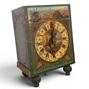 Puede incluir: Un reloj rectangular antiguo con una escena de paisaje pintada en la esfera y la parte superior. La esfera del reloj presenta números romanos y manecillas ornamentadas. El reloj es de color verde oscuro con detalles florales y descansa sobre cuatro pequeños pies oscuros.