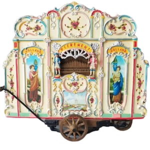Puede incluir: Una caja de música decorativa de estilo antiguo con forma de órgano callejero holandés. La caja de color crema presenta adornos ornamentados, detalles florales y escenas pintadas. La palabra "PIEREMENT" se muestra en la parte superior. El órgano tiene una rueda de madera.