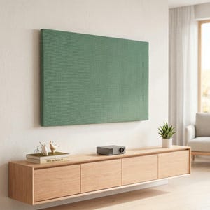Puede incluir: Un panel grande, rectangular, verde salvia con un patrón texturizado en forma de rejilla está montado en una pared blanca. Debajo, una consola multimedia flotante de madera clara con cuatro cajones contiene un pequeño proyector, una planta en maceta y objetos decorativos.