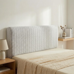 May include: A rectangular bed headboard featuring a grey and white chevron design. The headboard is padded, with a neutral-toned bedspread. A wooden bedside table with a lamp is also visible.