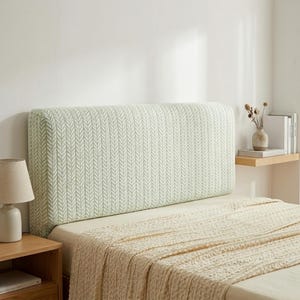 May include: A headboard with a light green and white chevron pattern. The bed is covered with a beige blanket. A small wooden bedside table and lamp are on the left. The headboard measures approximately 150cm in width.