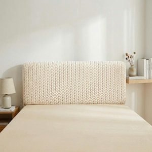 May include: A beige headboard with a repeating arrow pattern, positioned on a bed with a matching beige sheet. The rectangular headboard provides a decorative feature in the bedroom. A small lamp and side table are visible.