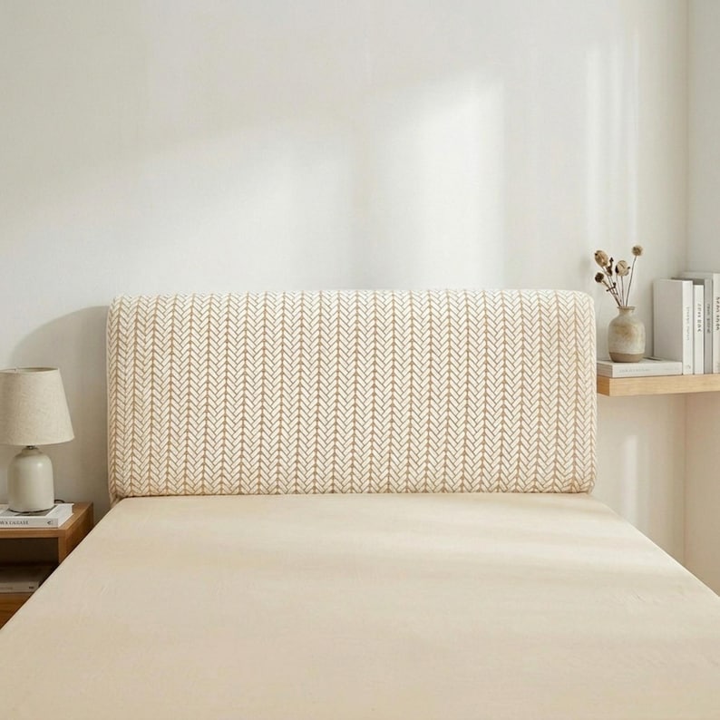 May include: A beige headboard with a repeating arrow pattern, positioned on a bed with a matching beige sheet. The rectangular headboard provides a decorative feature in the bedroom. A small lamp and side table are visible.